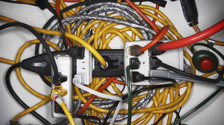 Múltiples cables de alimentación y cables de extensión enchufados en una base con múltiples tomacorrientes.