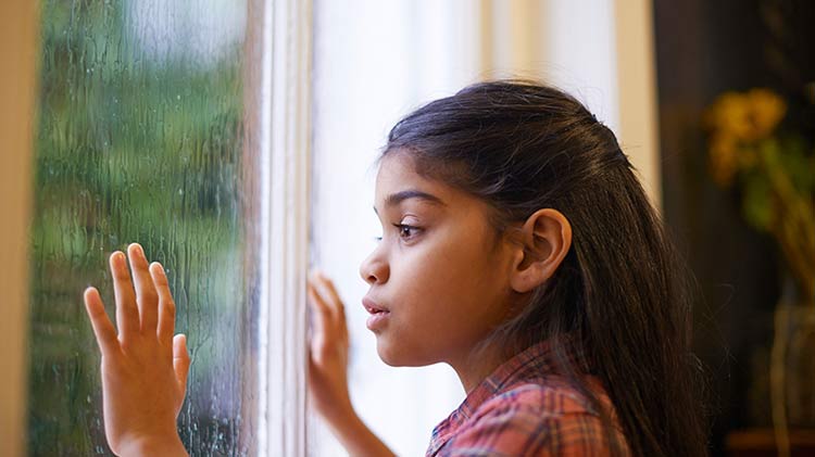 Una niña mira prudentemente la lluvia por la ventana.