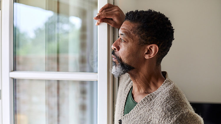 Un hombre mirando por una ventana pensando en su situación financiera tras su divorcio
