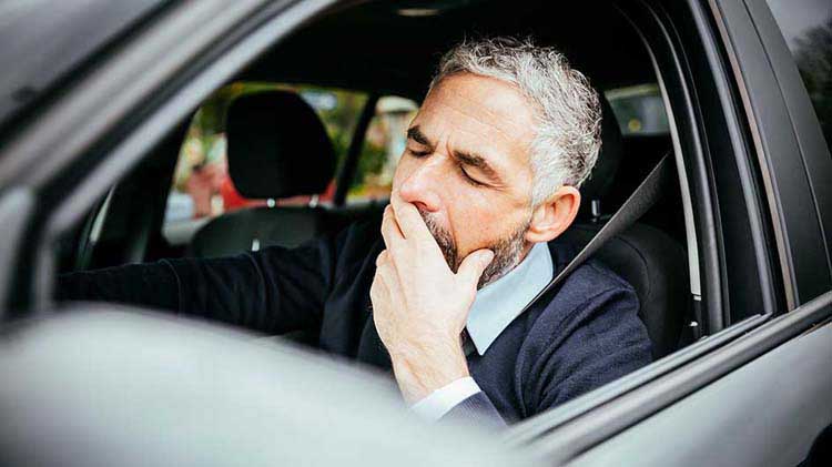Hombre bostezando en el timón del carro tratando de no quedarse dormido