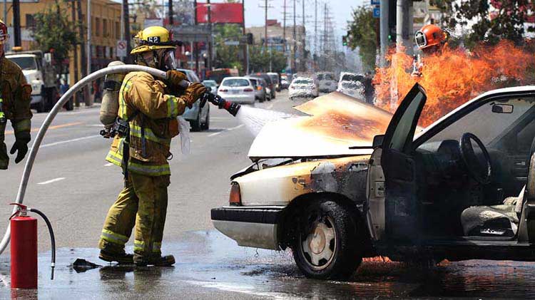 Un bombero rocía agua debajo del capó de un carro en llamas.
