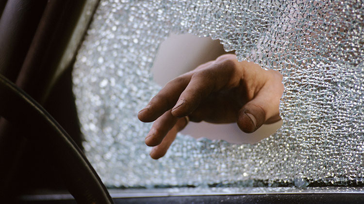 Un ladrón rompiendo la ventana de un carro mientras intenta entrar al vehículo.