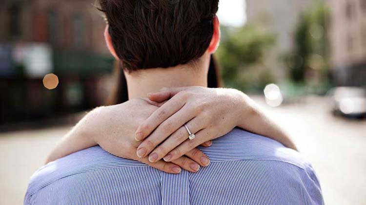 Manos con un anillo de compromiso abrazando a un hombre.