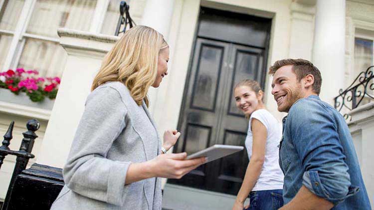 Agente de bienes raíces hablando con una pareja joven en un porche delantero.