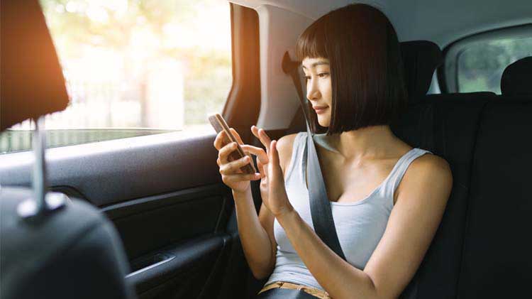 Imagen de una mujer sentada en un automóvil usando un teléfono celular.