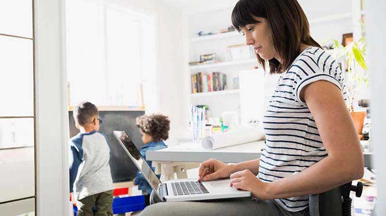 Mujer en el computador portátil y niños al fondo.