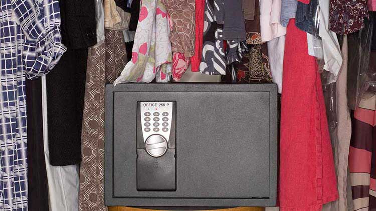 Una caja fuerte puesta entre la ropa colgada en un armario.