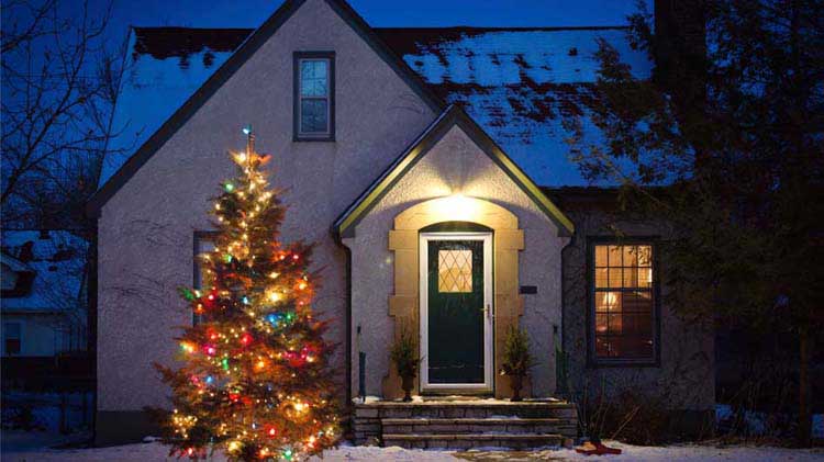 Acogedora casa con un árbol de Navidad iluminado en el exterior, al atardecer.