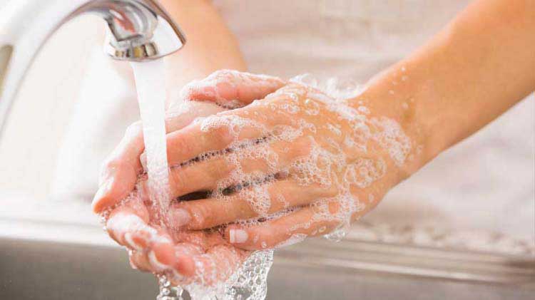 Persona que se lava las manos con pompas de jabón debajo de un grifo en funcionamiento.