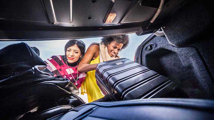 Mujeres metiendo maletas en el maletero del carro