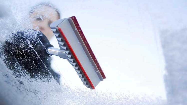 Persona quitando nieve y hielo de su parabrisas en el invierno.