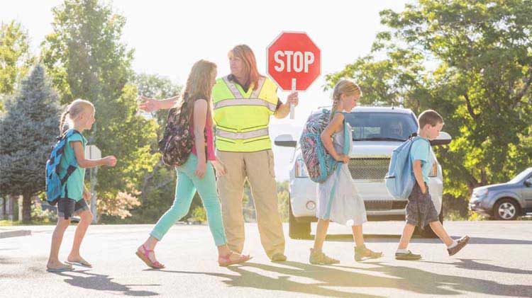Un guardia de cruce escolar ayuda a unos niños a cruzar la calle.