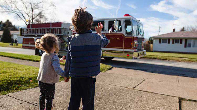 Niños saludan con sus manos a un camión de bomberos