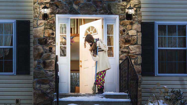 Mujer limpia nieve del pórtico de su casa con las luces encendidas