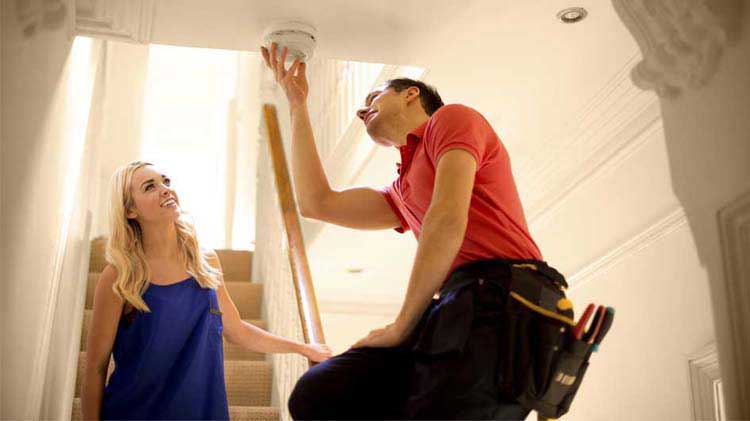 Mujer observando a un hombre instalar un detector de humo.