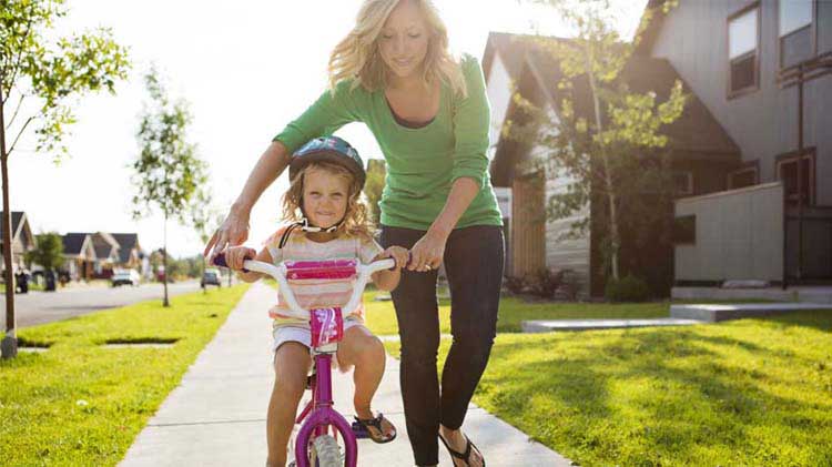 Una mamá ayuda a su hija a aprender a montar bicicleta.