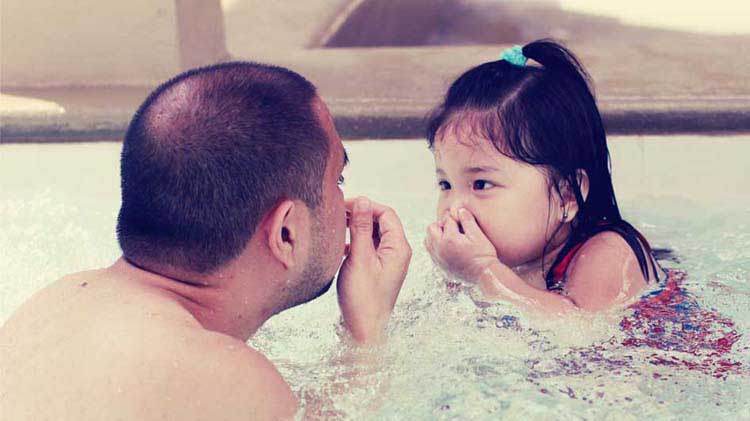 Un padre practica con su hija cómo sumergirse en el agua.