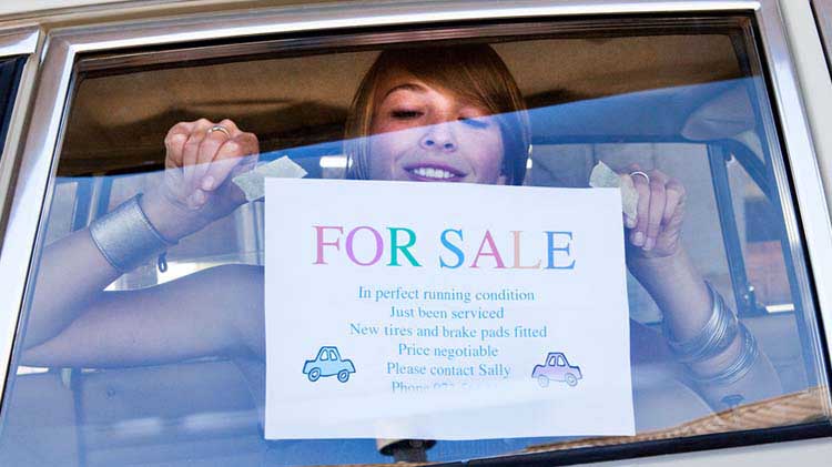 Mujer colgando un cartel de venta casero en la ventana del carro