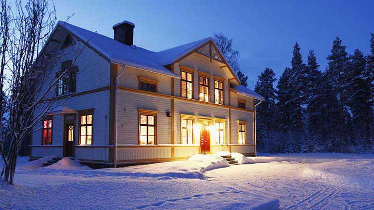 Una casa bien iluminada al atardecer en un ambiente cubierto de nieve