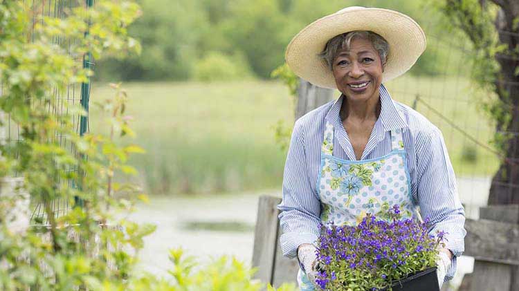 Mujer con sombrero sosteniendo plantas en el jardín