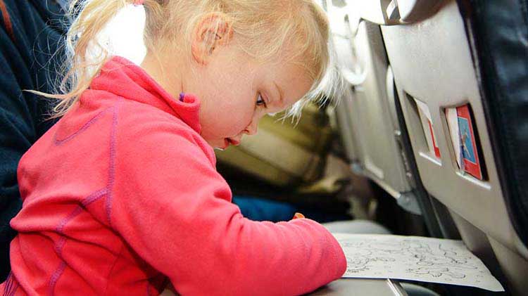 Una niña colorea un dibujo en una mesa plegable mientras vuela segura en un avión.