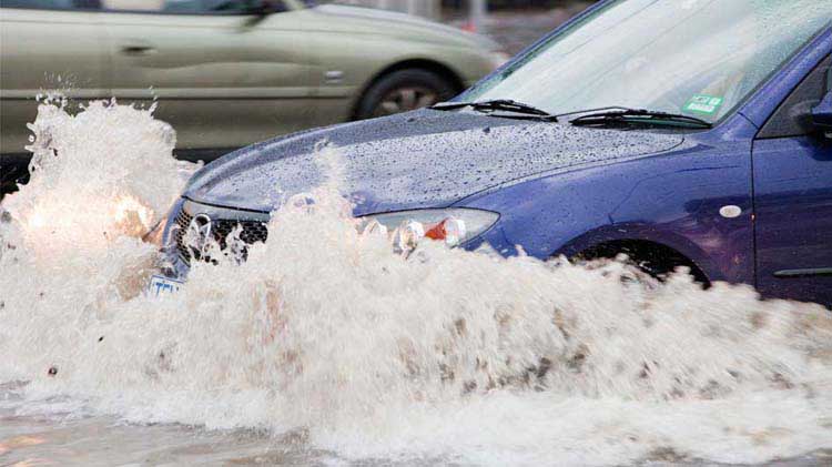 Carro circulando por una calle inundada y posiblemente sufriendo daños por inundación como resultado..