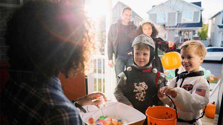 Usando consejos de seguridad para Halloween, un niño disfrazado de caballero medieval y otro de astronauta reciben dulces.