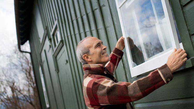 Hombre arreglando ventana en el exterior de una casa histórica para mantenimiento.