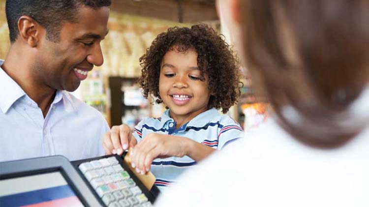 Un padre deja que su hijo pequeño sostenga su tarjeta de crédito para pasarla por la caja registradora de una tienda.