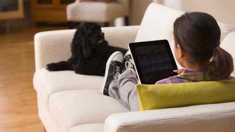 Un niño solo en el sofá mirando una tableta.