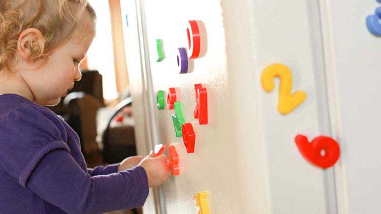 Niño pequeño jugando con imanes de refrigerador que podrían ser un riesgo en el hogar.