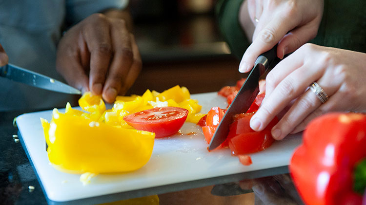 Una pareja está cortando pimientos y tomates orgánicos.