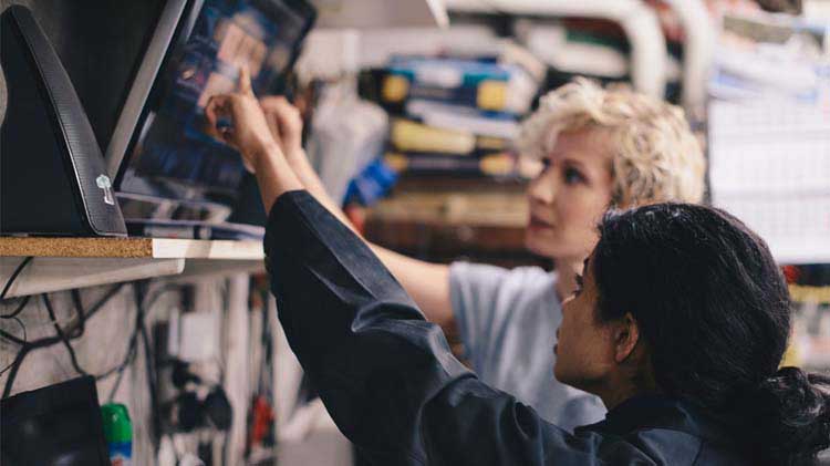 Dos mujeres discuten problemas mecánicos en un taller señalando un monitor.
