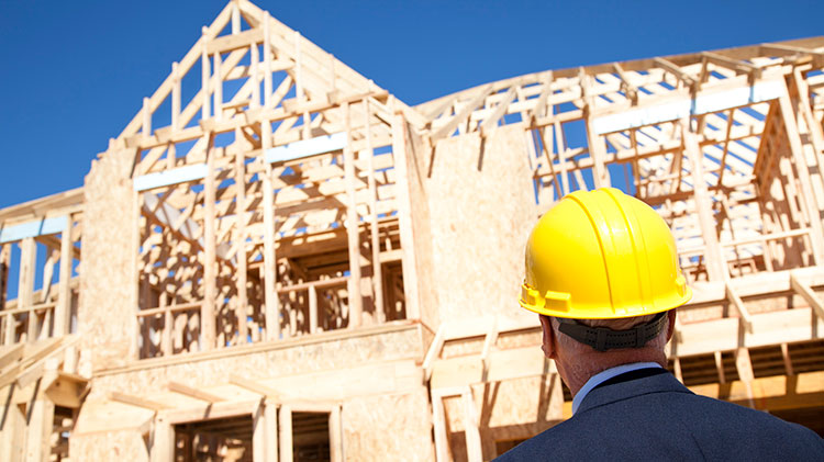 Un hombre de casco amarillo mira la obra mientras construyen una nueva vivienda con armazón de madera.