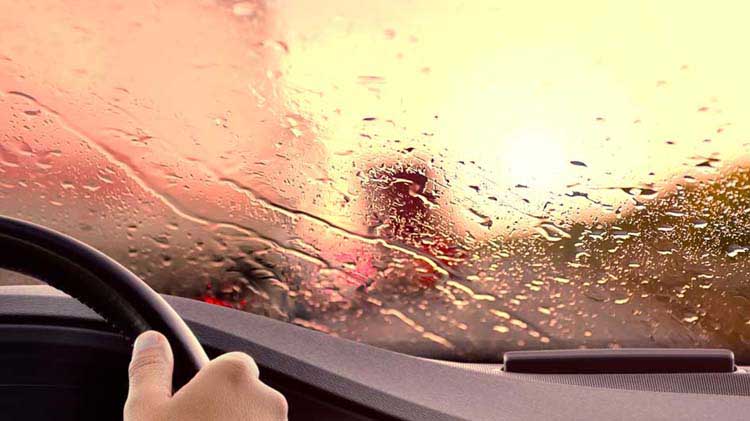 Escena borrosa de la carretera mostrada a través del parabrisas cubierto de lluvia.