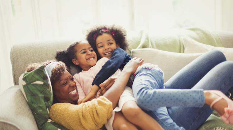 Una mujer y dos niñas tumbadas en un sofá, juntas y contentas