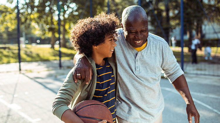 El niño lleva una pelota de baloncesto y camina del brazo con su abuelo a través de una cancha de baloncesto.