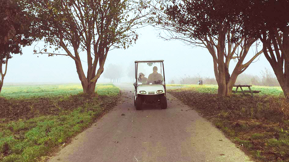 Hombre y niño en un campo de golf neblinoso manejando un carrito de golf.
