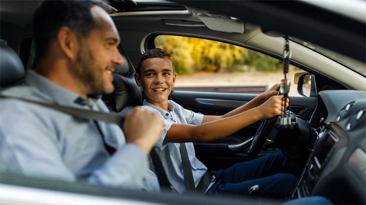 Un padre se abrocha el cinturón de seguridad, sentado en el primer carro de su hijo adolescente.