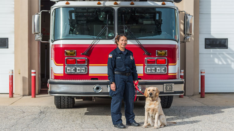 Maggie Greene, la primera latina en graduarse del programa de perros para la investigación de incendios provocados de State Farm, junto a un camión de bomberos con su compañera canina, Hannah. 