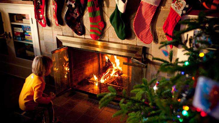 Un niño mira una chimenea encendida que tiene medias navideñas encima.