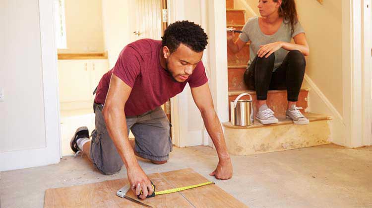 Un hombre mide una tabla en el piso mientras que una mujer pinta una pared para completar la renovación de su vivienda al estilo &quot;hazlo tú mismo&quot;.