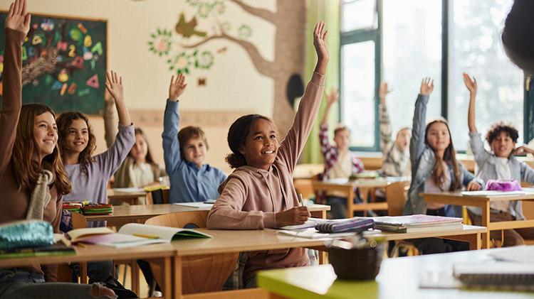 Elementary students raising their hands in class at school.