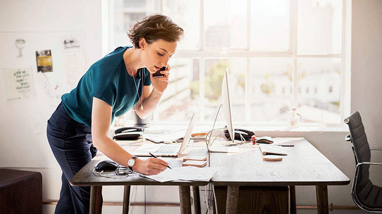 Mujer hablando por teléfono junto a una mesa de trabajo.