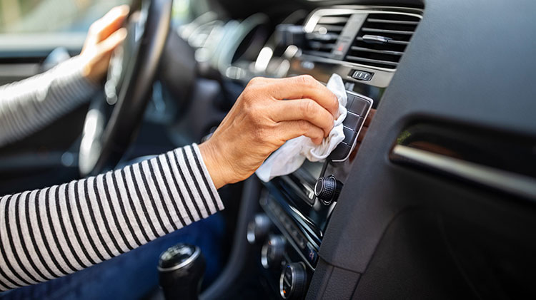 Una mujer limpia con una toalla el conducto de ventilación del tablero de su carro.