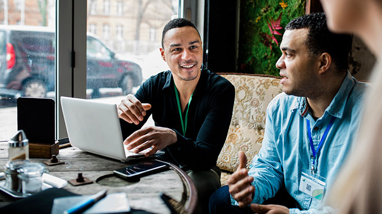 Dos hombres hablando y trabajando en una computadora portátil.