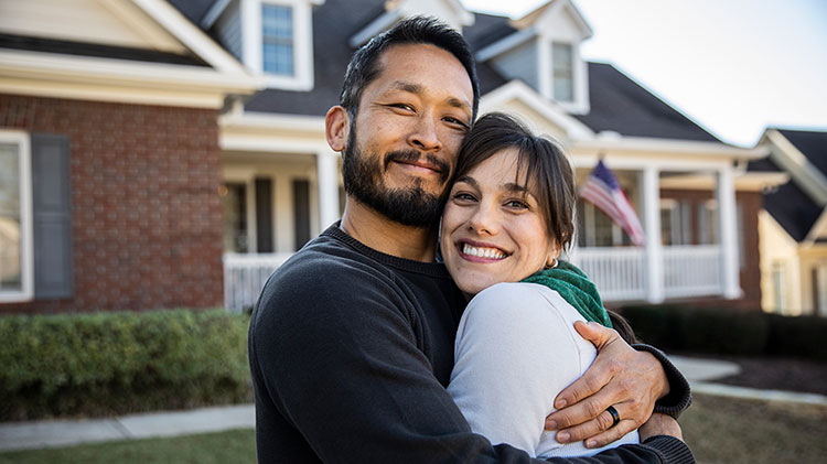 Una pareja abrazada frente a su casa.