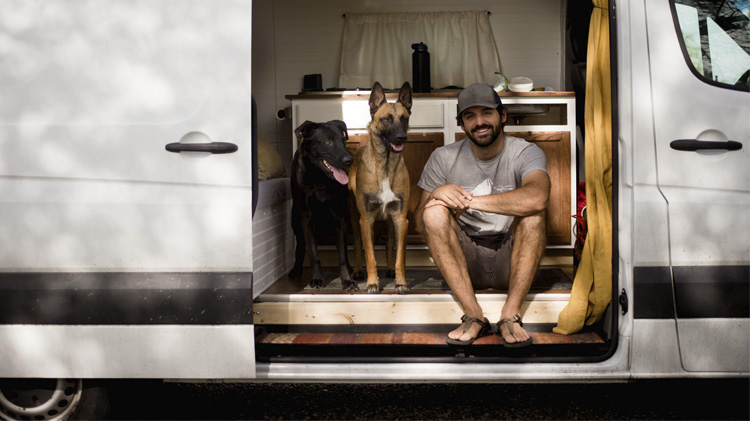 Un hombre sonriente sentado con sus perros en una casa rodante