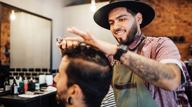 Un barbero sonriendo, cortando el pelo de un cliente en un salón.