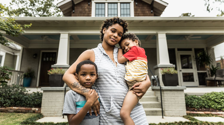 Retrato de una madre con sus hijos pequeños frente a una casa. 